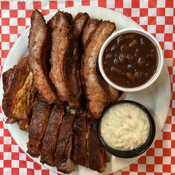 A plate of Terrell's BBQ ribs with sides of baked beans and coleslaw on a red and white checkered tablecloth.