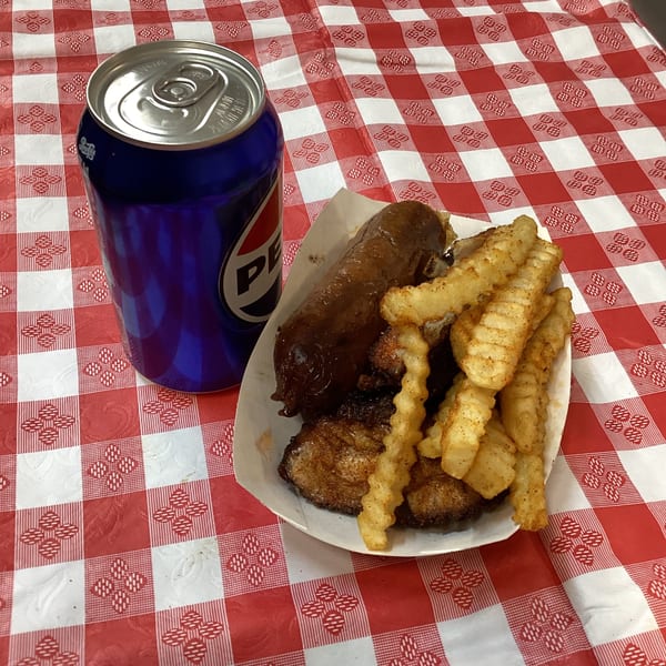 Terrell's Eat The Bone BBQ sausage, ribs, and crinkle-cut fries with a Pepsi on a red and white checkered tablecloth.